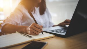 A person with a laptop taking notes