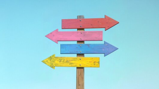 Wegweiser aus Holz mit bunten Pfeilen in verschiedene Richtungen.